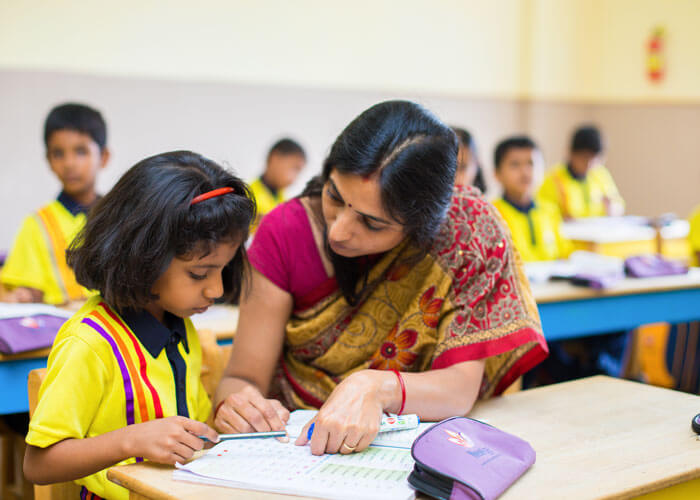 Teacher helping a student during a classroom activity at NewAge World School.