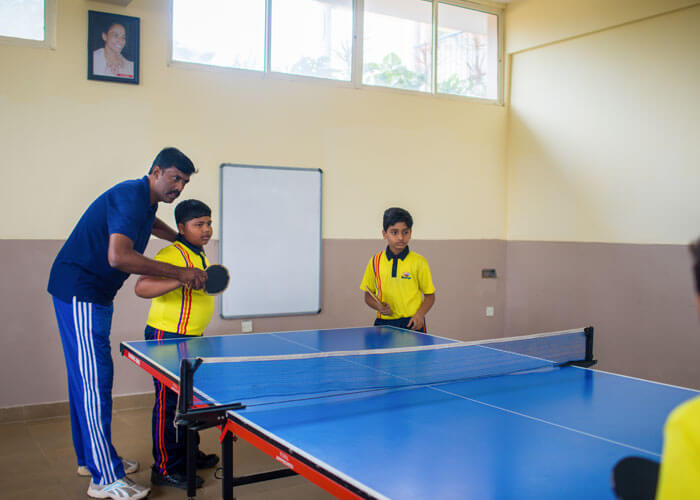Teacher guiding students during a table tennis session at NewAge World School.