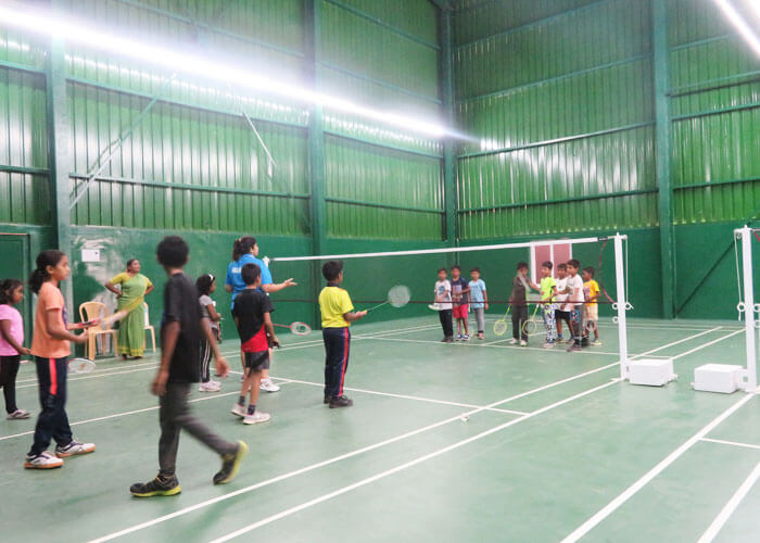 Students learning badminton skills in a group session at NewAge World School's indoor court.
